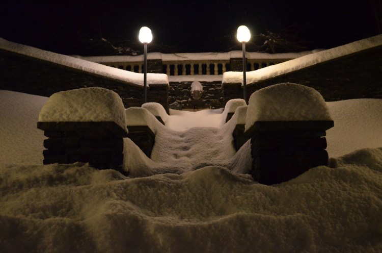On Goddard College Campus, view up snow covered steps, flanked by stone columns also topped by deep snow with building up at top of stairwell.