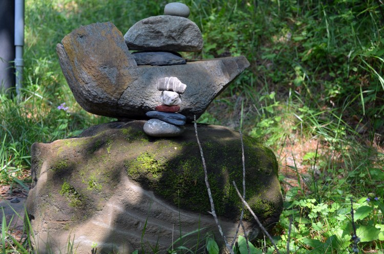 Large cairn built of boulders in sun-dappled wood has a small cairn nestled amongst the larger rocks.